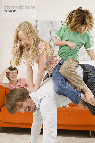 Junge (6-7) und Mädchen (8-9) auf dem Rücken des Vaters im Wohnzimmer