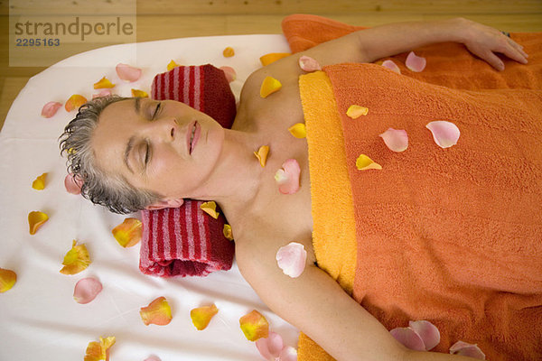 Reife Frau auf Massageliege mit Blütenblättern  Portrait