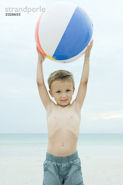 Kleiner Junge am Strand  hält den Strandball hoch  lächelt die Kamera an.
