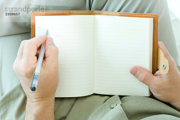 Mann schreibt in Tagebuch  abgeschnittene Ansicht der Hände