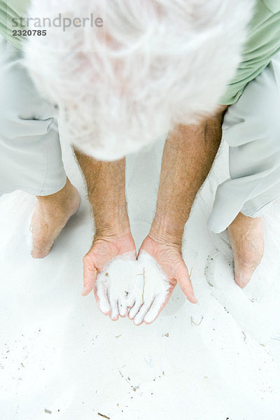 Mann bückt sich  hält Sand in beiden Händen  hoher Blickwinkel