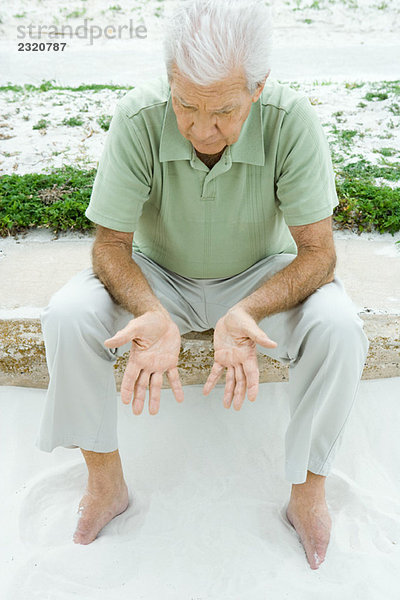 Mann am Strand sitzend  auf die Hände blickend  hohe Blickwinkel