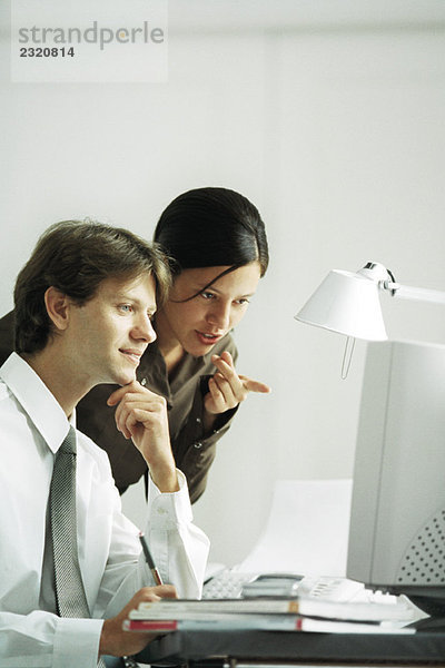 Männliche und weibliche Kollegen  die zusammen auf den Computer schauen  die Frau zeigt