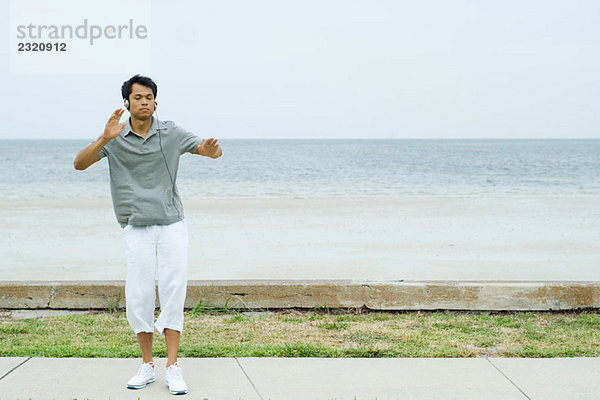 Mann steht mit ausgestreckten Armen am Strand  hört Kopfhörer  Augen zu.