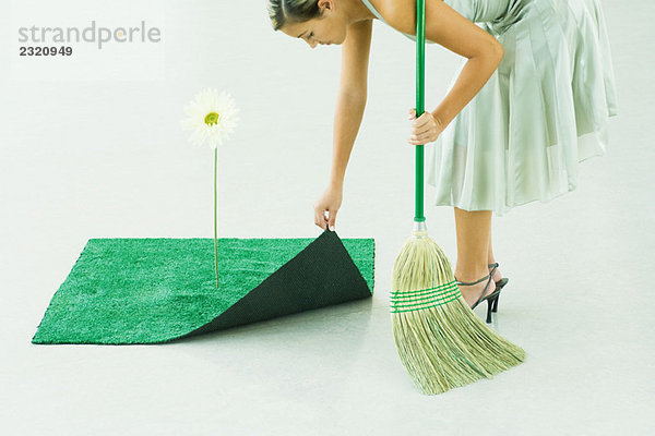 Frau bückt sich  Besen in der Hand  Hebeecke aus Kunstrasen neben Gerbera Daisy