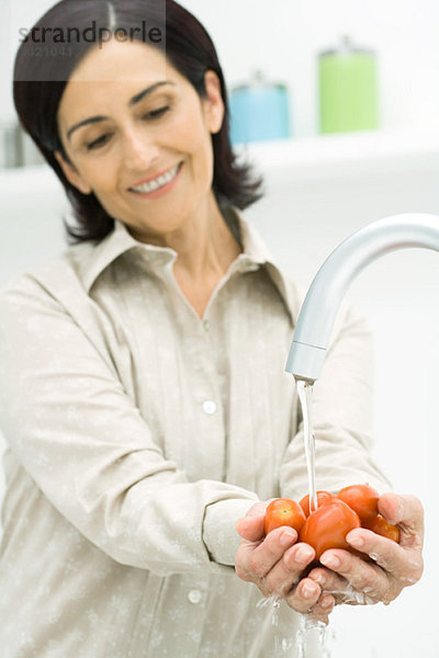 Frau hebt eine Handvoll Tomaten unter dem Wasserhahn auf  lächelnd