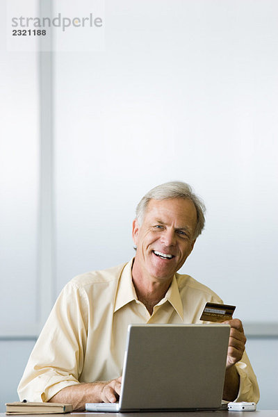 Mann mit Laptop-Computer  mit Kreditkarte  lächelnd in der Kamera