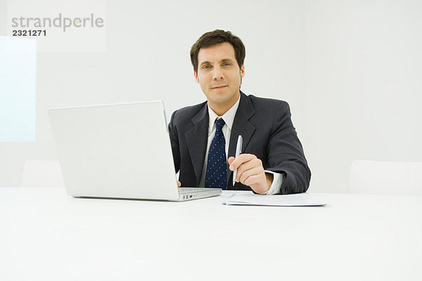 Geschäftsmann am Schreibtisch sitzend  mit Laptop-Computer  lächelnd vor der Kamera