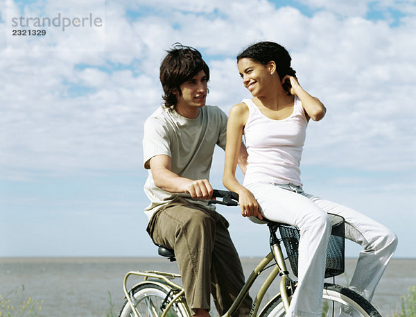 Junges Paar auf dem Fahrrad  Frau auf dem Lenker sitzend  über die Schulter schauend