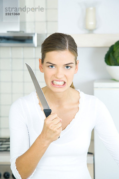 Frau hält Küchenmesser hoch  Zähne zusammenbeißen  Blick in die Kamera  Porträt