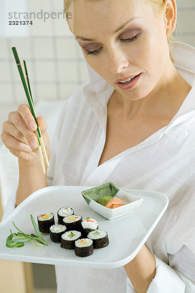 Frau hält Maki-Sushi und Essstäbchen und schaut nach unten.