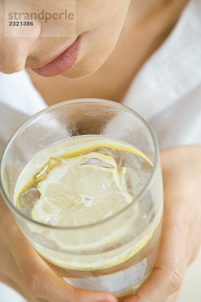 Frau hält Wasserglas mit schwimmender Zitronenscheibe  Nahaufnahme  beschnitten