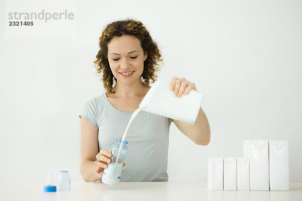 Frau gießt Milch aus dem Karton in die Babyflasche  lächelnd