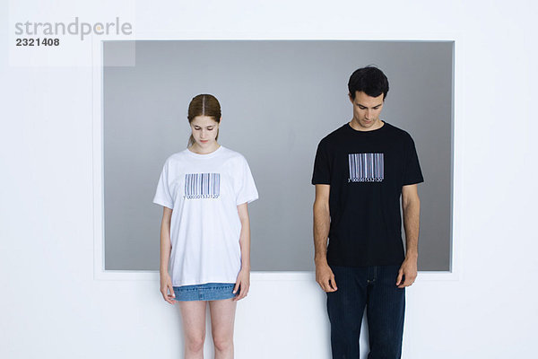 Zwei junge Erwachsene in T-Shirts mit Barcodes bedruckt  beide mit Blick nach unten.