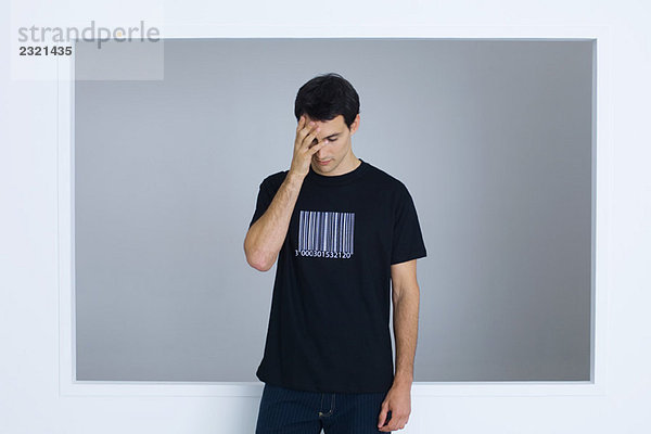 Mann im T-Shirt mit Barcode bedruckt  Gesicht mit Hand bedeckt