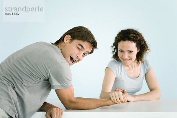 Paar Armdrücken  beide schauen in die Kamera  der Mann zwinkert  während er die Frau gewinnen lässt.