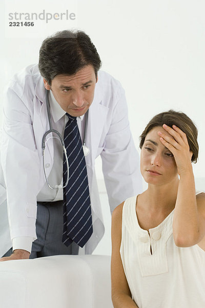 Frau sitzend  den Kopf haltend  Ärztin hinter sich beugend