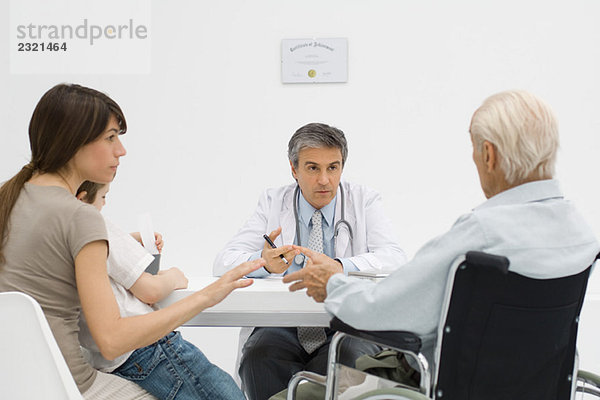 Arzt am Schreibtisch im Gespräch mit dem älteren Patienten und seiner Familie