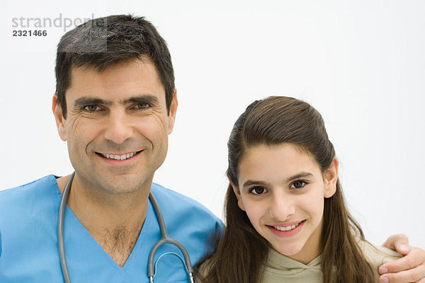 Männlicher Arzt mit Arm um die Schulter des Mädchens  beide lächelnd vor der Kamera  Porträt