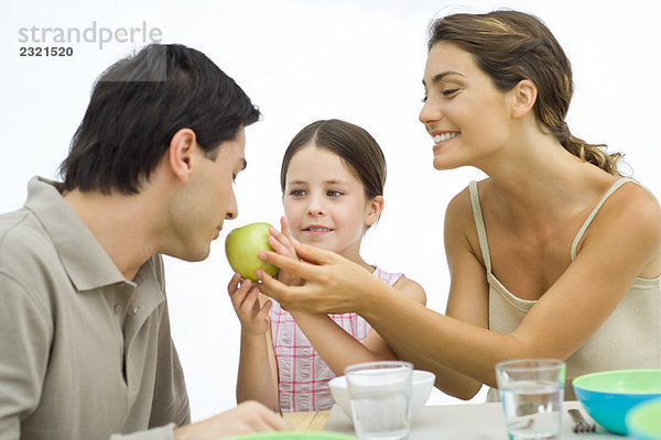 Familie der gesunden Esser  Mutter und Tochter halten den Apfel dem Vater entgegen.