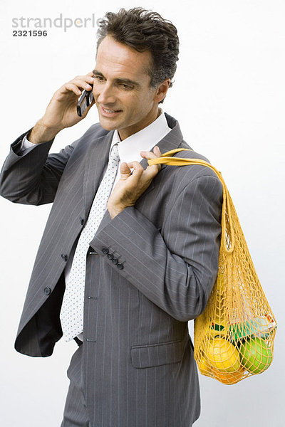 Geschäftsmann hält wiederverwendbare Einkaufstasche über die Schulter  per Handy