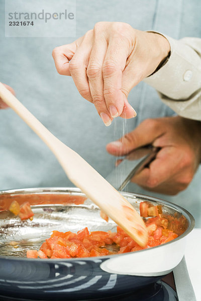Gemeinsames Kochen  Frau streut Salz in die Pfanne  Ausschnittansicht