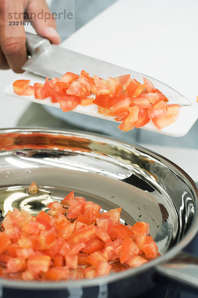 Mann schabt gewürfelte Tomaten mit Messer in den Topf  Schnittansicht