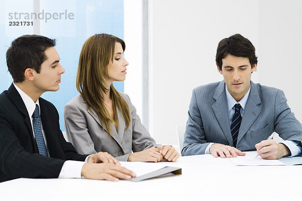 Geschäftsfreunde bei der Besprechung  Mann unterschreibt Dokument  während andere zusehen.