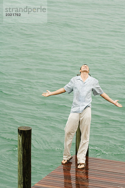 Mann lehnt sich im Regen auf den Pier zurück  Arme ausstrecken  Augen geschlossen  Hochwinkelansicht