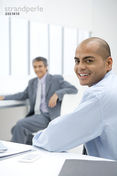 Zwei Geschäftsleute sitzen im Büro und lächeln vor der Kamera.