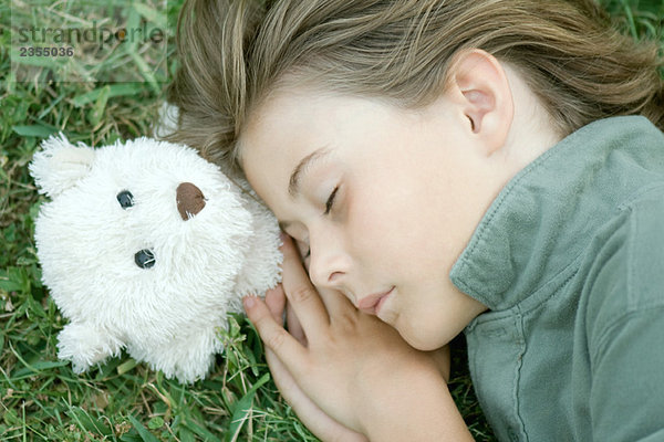 Junge im Gras liegend mit geschlossenen Augen  Kopf auf Teddybär ruhend