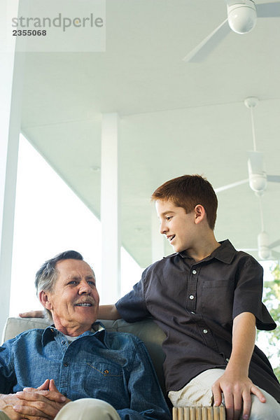 Großvater und Enkel sitzen zusammen auf der Veranda  beide lächelnd.