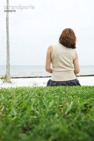 Frau auf dem Boden sitzend  Blick aufs Meer  Rückansicht
