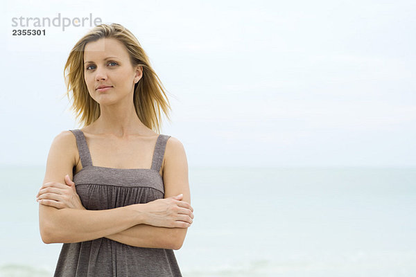 Blonde Frau stehend mit gefalteten Armen  Meer im Hintergrund  Blick auf Kamera  Taille oben