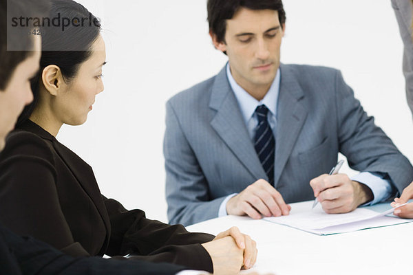 Geschäftspartner am Tisch sitzend  ein Mann unterschreibt Dokument