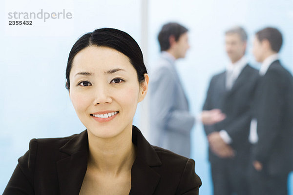 Geschäftsfrau lächelt in die Kamera  männliche Kollegen stehen im Hintergrund