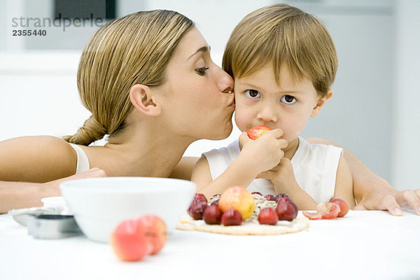 Frau küsst kleinen Jungen auf Wange  Junge isst Apfel