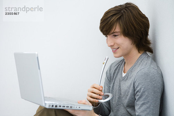 Junger Mann schaut auf den Laptop  spricht ins Mikrofon  Seitenansicht