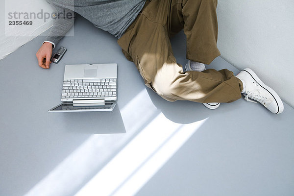 Junger Mann auf dem Boden vor dem Laptop sitzend  abgeschnittene Ansicht