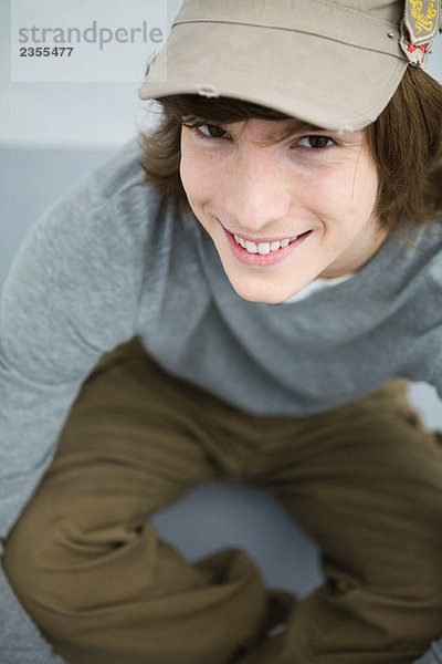 Junger Mann auf dem Boden sitzend  lächelnd vor der Kamera  hoher Blickwinkel