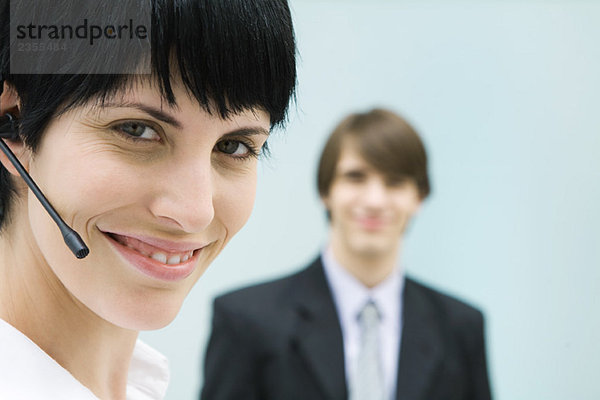 Frau mit Headset  lächelnd vor der Kamera  Geschäftsmann im Hintergrund