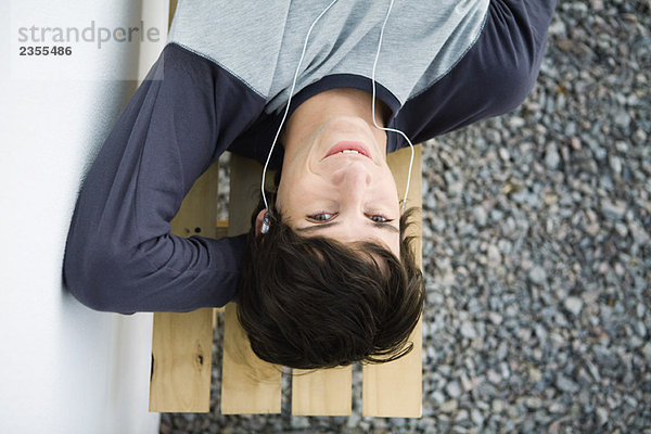 Junger Mann auf der Bank liegend  Kopfhörer hörend  Kamera schauend