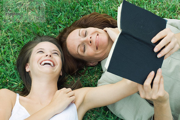 Mutter und Tochter liegen zusammen im Gras  lachend  Frau hält Buch