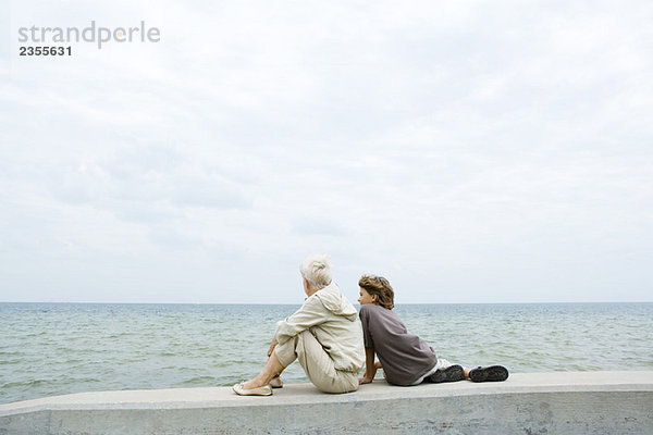 Großmutter und Enkel sitzen zusammen am Meer  Blick auf das Meer  Rückansicht