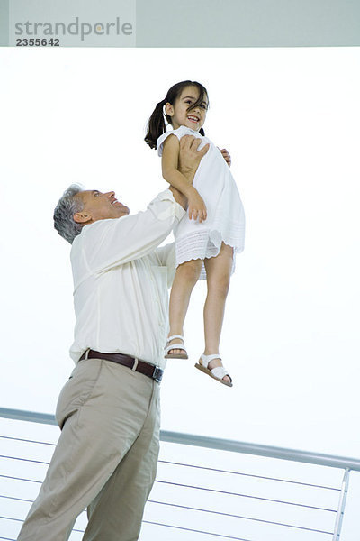Großvater hält Enkelin in der Luft  beide lächelnd  Blickwinkel niedrig