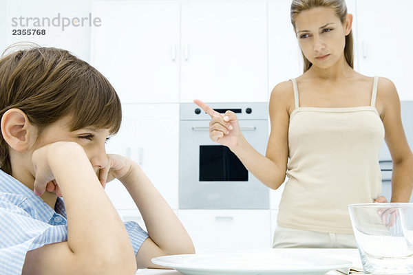 Junge schmollt am Küchentisch  Mutter schüttelt den Finger