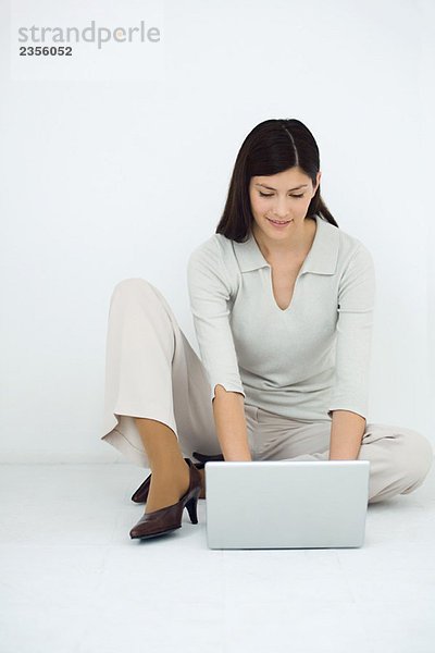 Frau auf dem Boden sitzend  mit Laptop-Computer  lächelnd