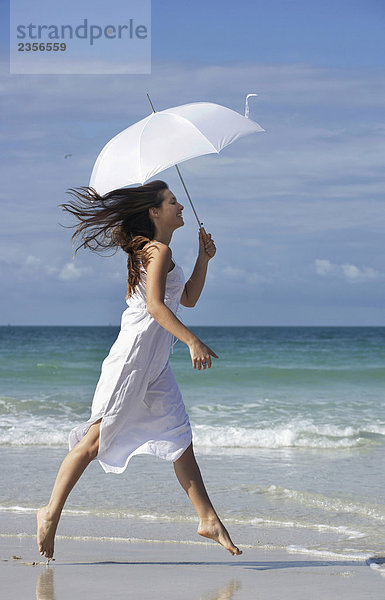 Frau mit Sonnenschirm am Strand überspringen