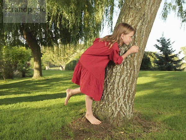 Junges Mädchen versteckt sich hinter einem Baum