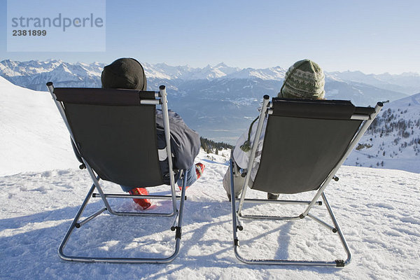 Mann  Frau entspannen auf Liegestühlen im Schnee